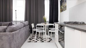 Una cocina moderna con zona de comedor, que incluye un sofá gris, sillas blancas y un tapete con estampado en blanco y negro.