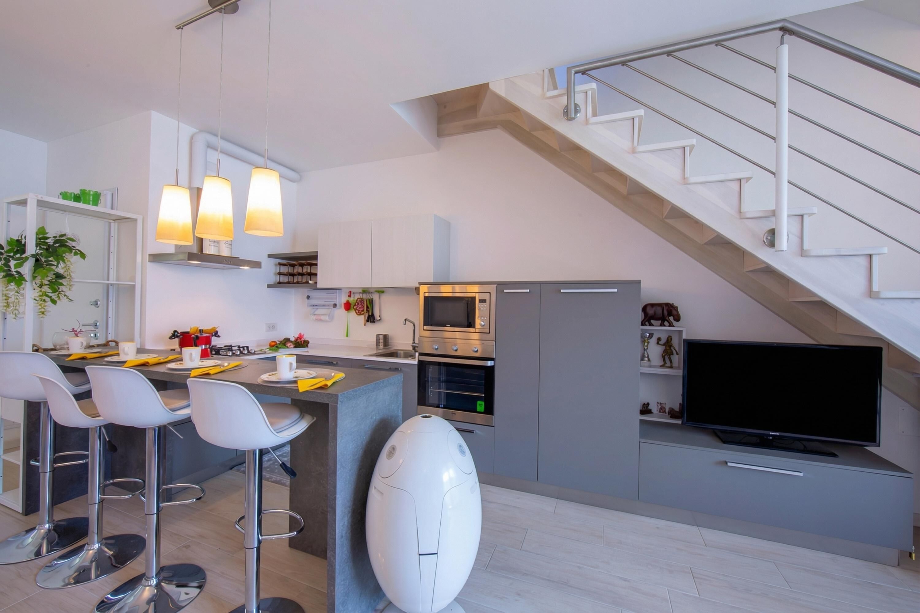 A modern kitchen with a central island, bar stools, a microwave, oven, and a flat-screen TV.