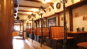 A row of wooden benches with striped cushions, a wooden floor, and a wall with framed pictures and a clock. - Hotel - Restaurant Franziskaner am Markt (Loningen)