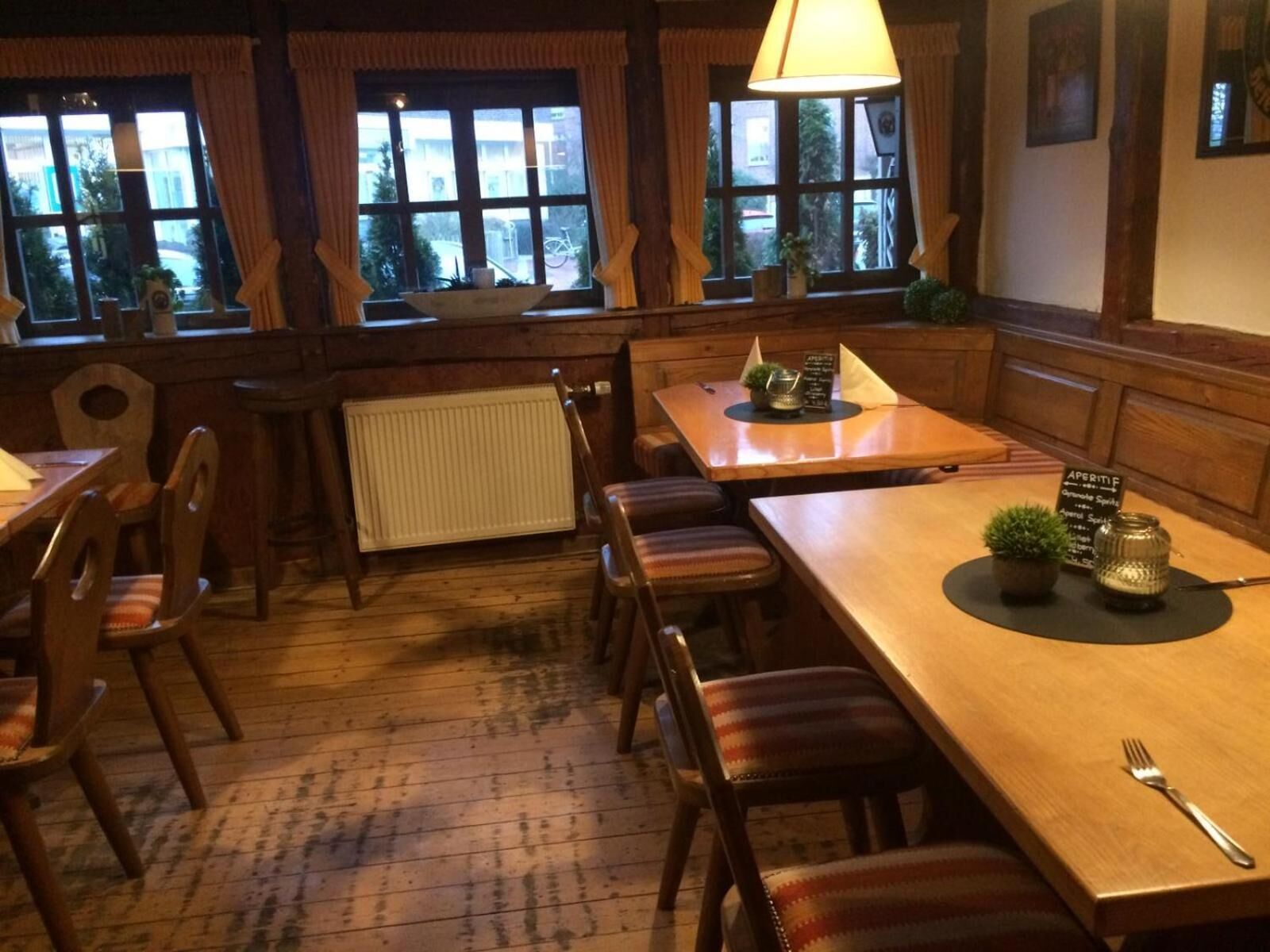 Un restaurant accueillant, avec des meubles en bois, de grandes fenêtres ornées de rideaux et une atmosphère chaleureuse.