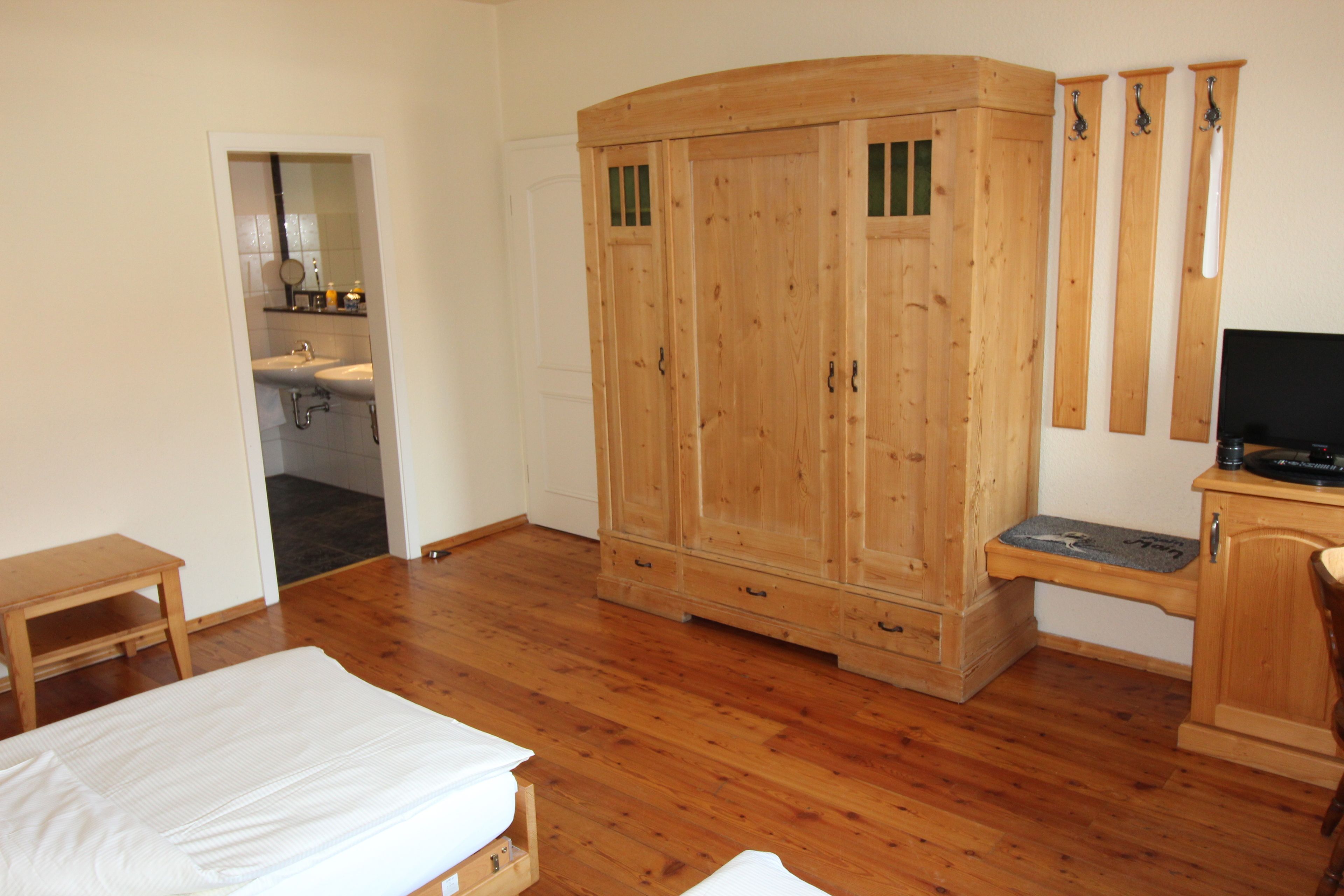 Un dormitorio con un armario de madera, una cama, una mesita y un escritorio con una silla.