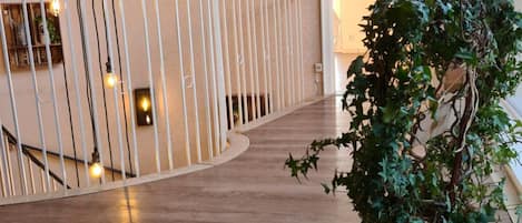 Un pasillo con piso de madera, baranda blanca y una planta en maceta.