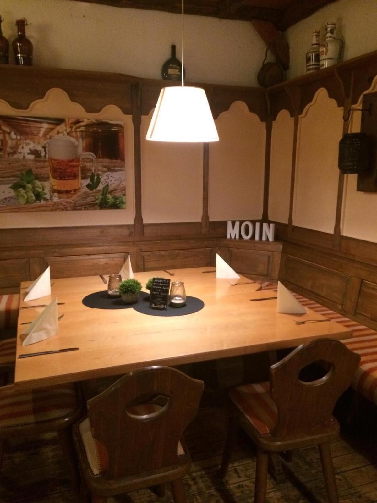 Ein Holztisch mit einer Pendelleuchte, umgeben von Holzstühlen. Ein Menügestell steht in der Mitte.