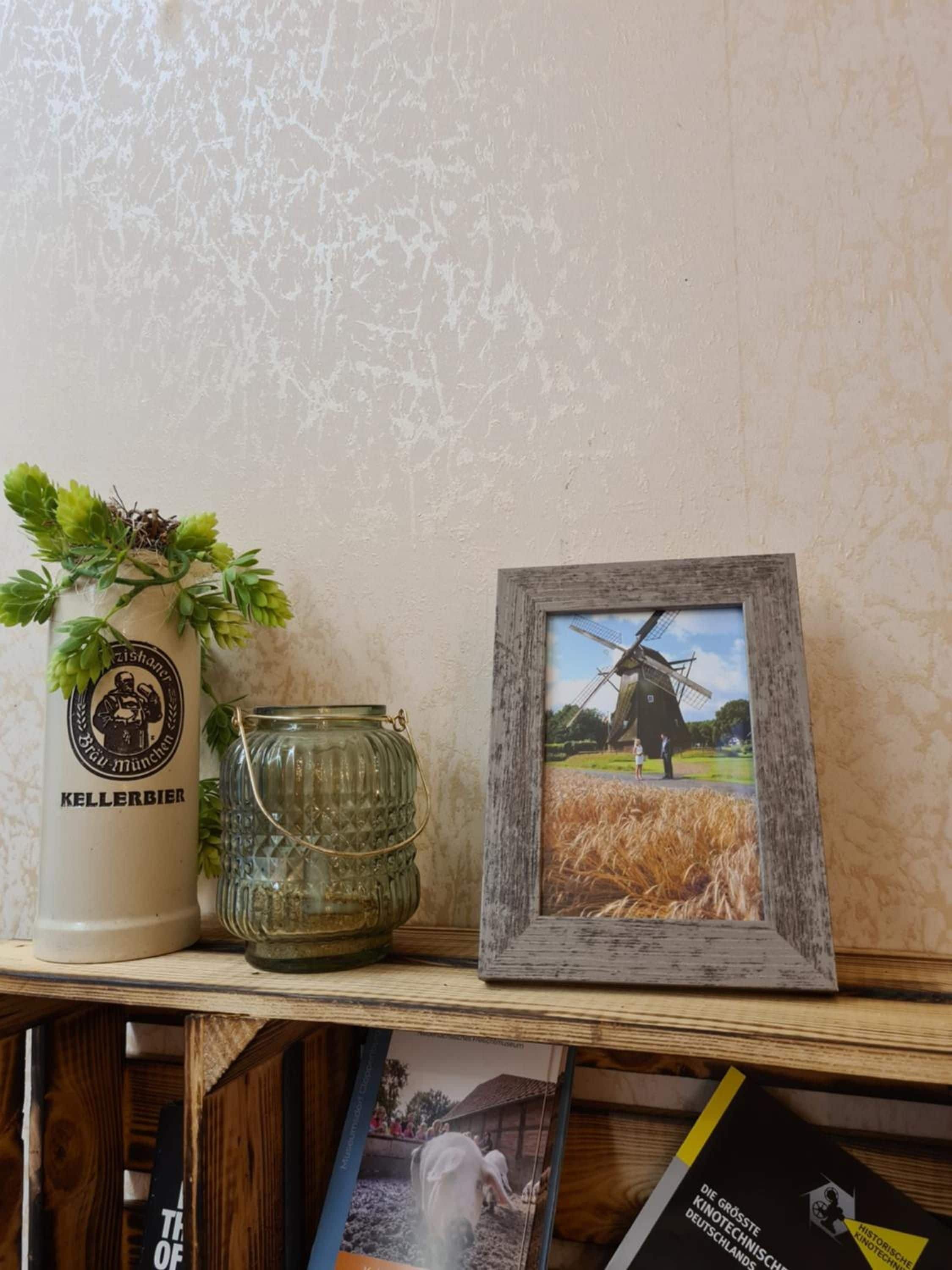 A shelf with a framed picture of a windmill, a glass jar, and a bottle with a label.