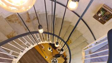Una escalera de caracol con una plataforma central de madera, barandillas de metal negro y lámparas colgantes.
