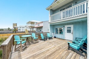 A wooden deck with turquoise Adirondack chairs and a small table, overlooking a beach.