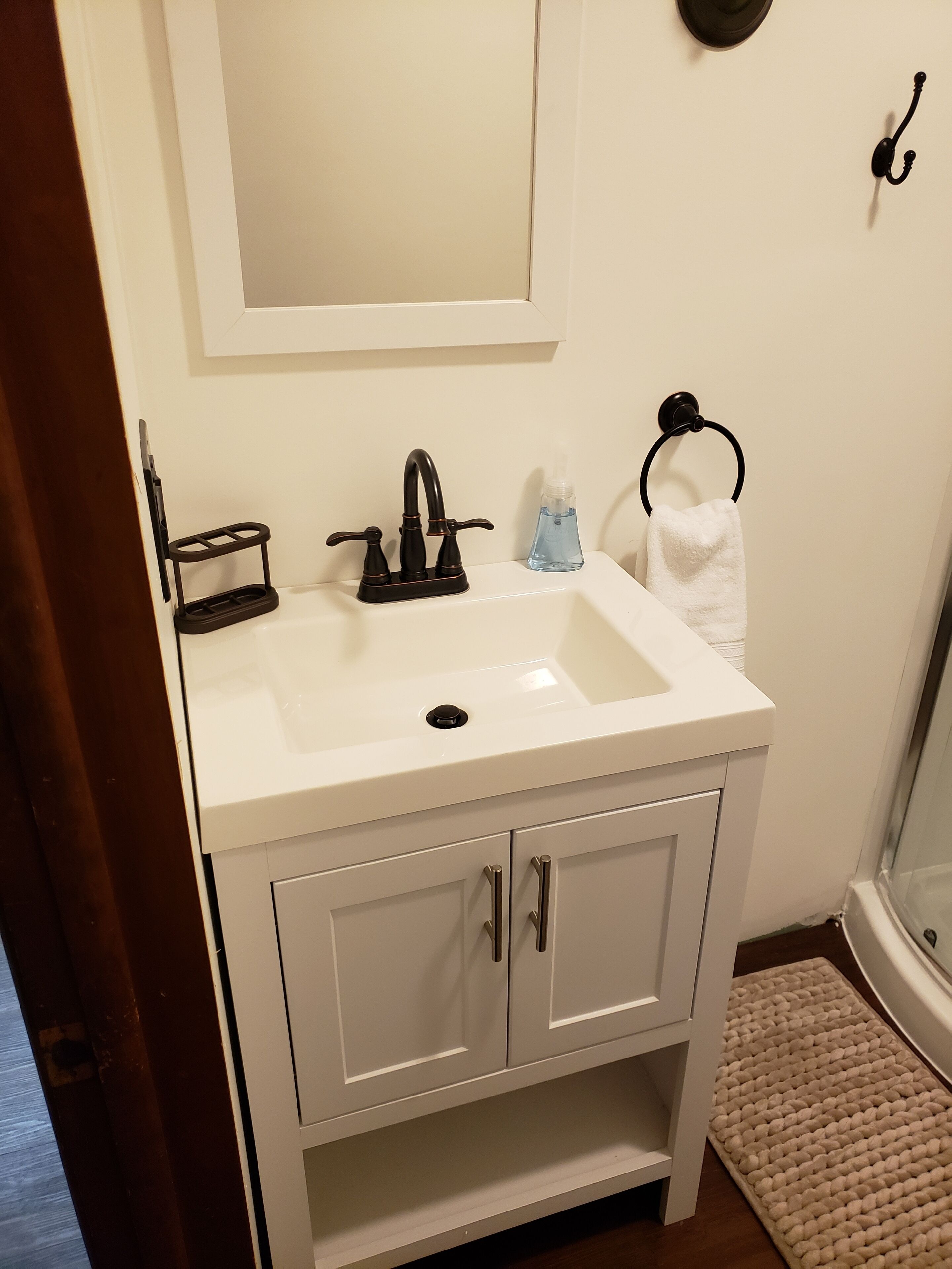 A bathroom with a white sink, a mirror above it, a towel ring, and a shower area.