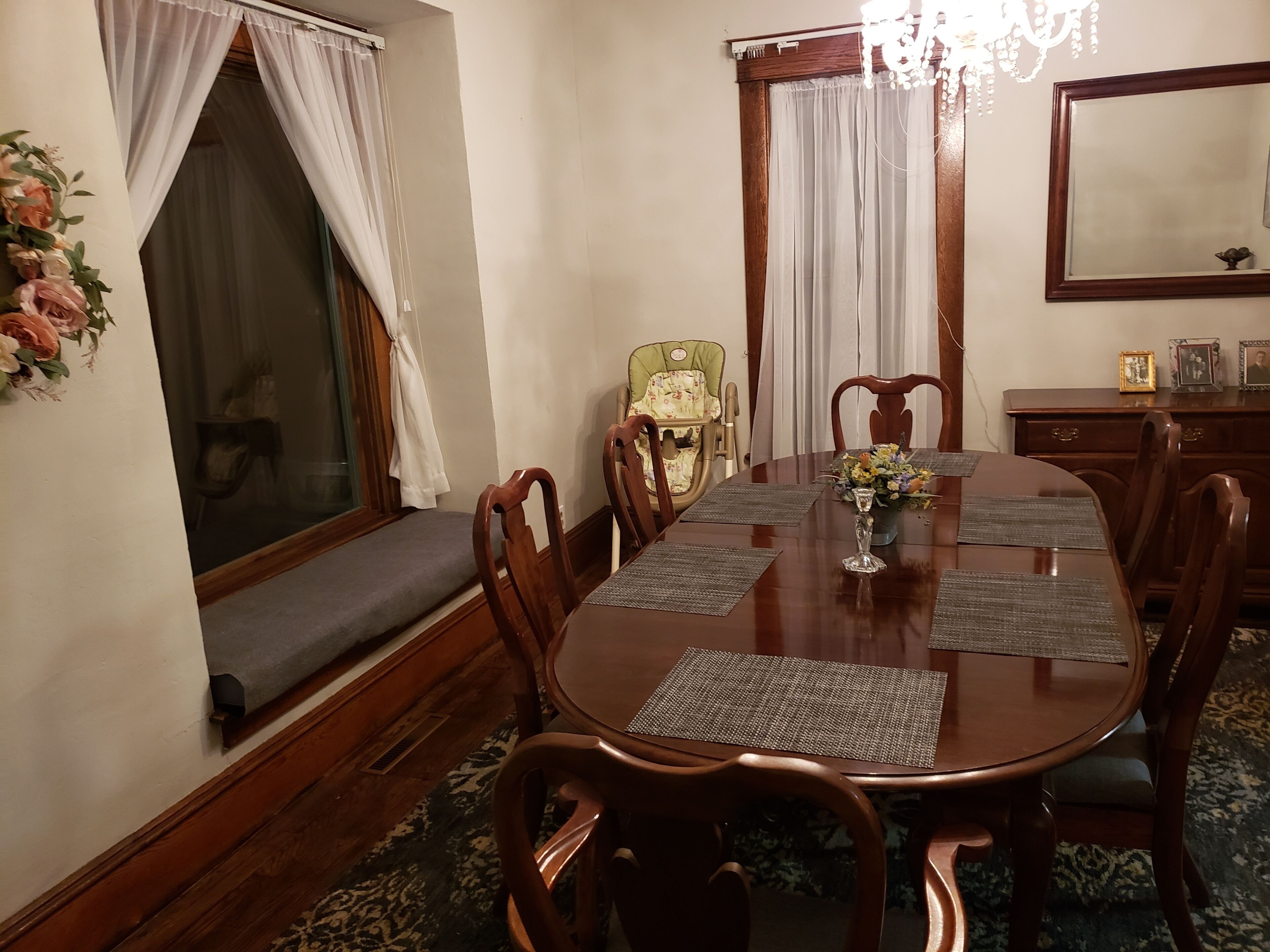 A dining room with a wooden table, chairs, a bench, and a window with curtains.