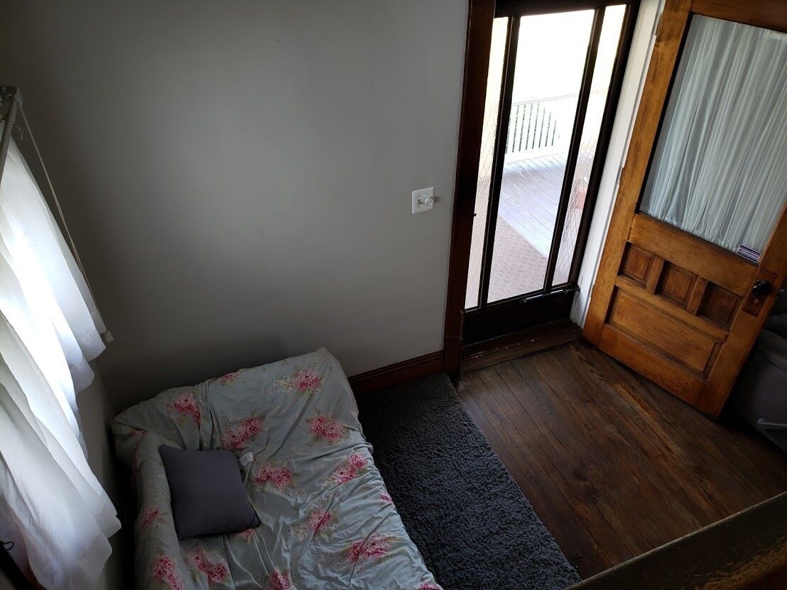 Une petite pièce avec une porte en bois, une fenêtre avec des rideaux, un canapé recouvert d’une housse à motifs floraux et un tapis sombre.