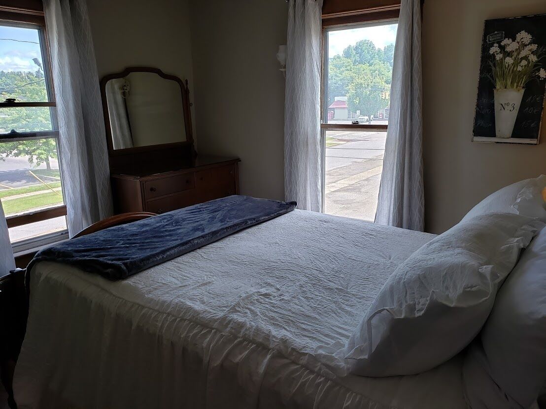 Une chambre à coucher avec un lit, une commode, un miroir et une fenêtre avec des rideaux.