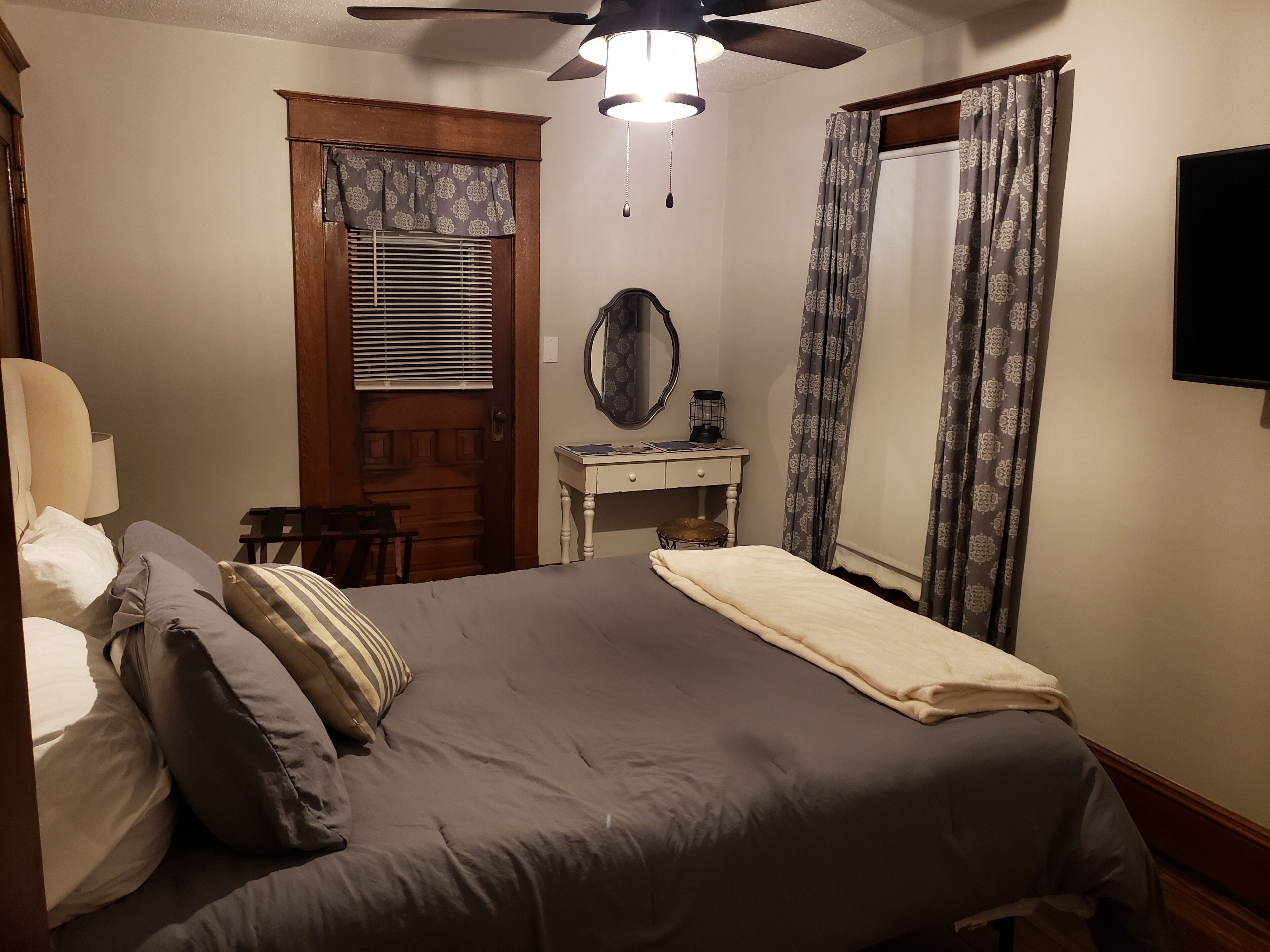 Ein Schlafzimmer mit Bett, Schreibtisch, Stuhl, Deckenventilator und Fernseher.