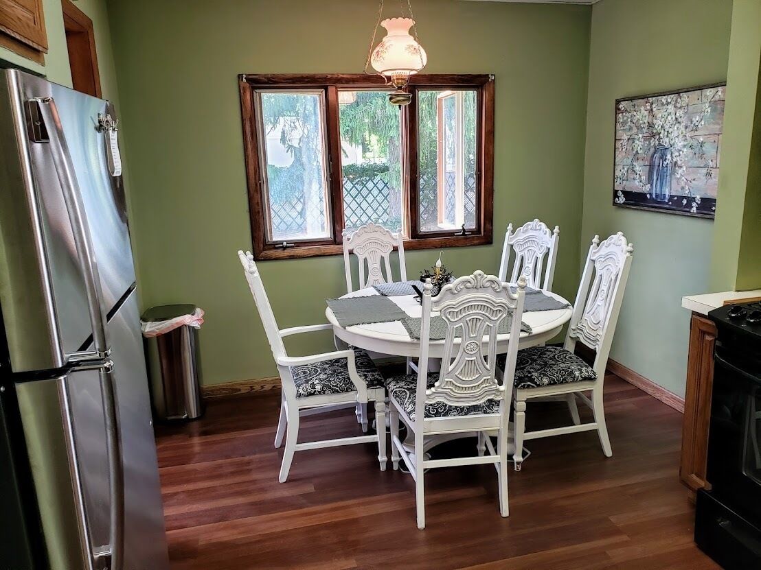 A dining area with a round table and white chairs, a refrigerator, and a stove.
