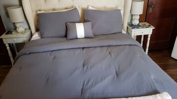 Un letto con testiera imbottita, biancheria grigia e due comodini con lampade.