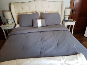 Un letto con testiera imbottita, biancheria grigia e due comodini con lampade.