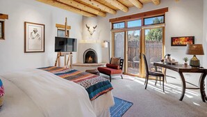 A bedroom with a large bed, a fireplace, a TV, and a desk with a lamp.