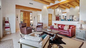 A spacious living room with a high wooden ceiling, leather sofas, a coffee table, and a rustic wooden floor.