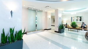 A modern lobby with a reception desk, seating area, and potted plants. - Beachfront Condo | Ocean Breeze & Resort Pool (Hollywood)