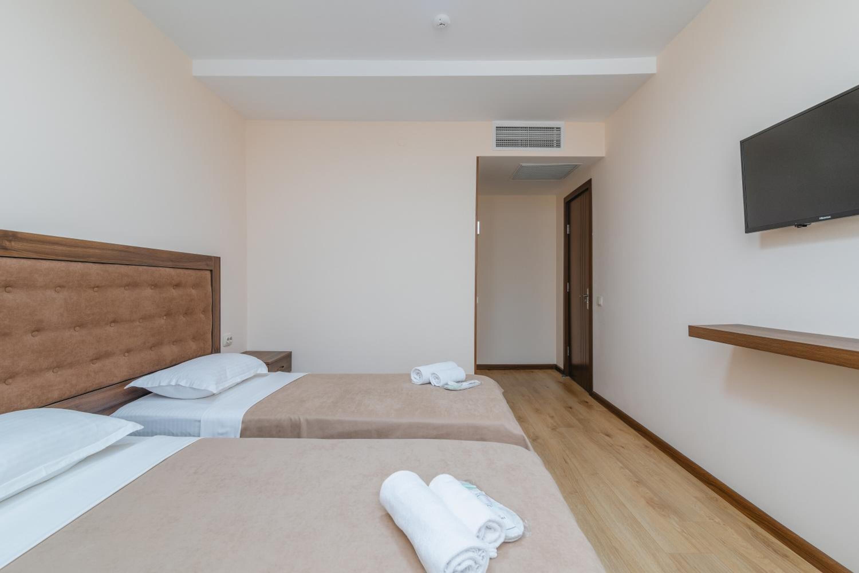 Camera d'albergo con due letti, una TV fissata alla parete e pavimento in legno.