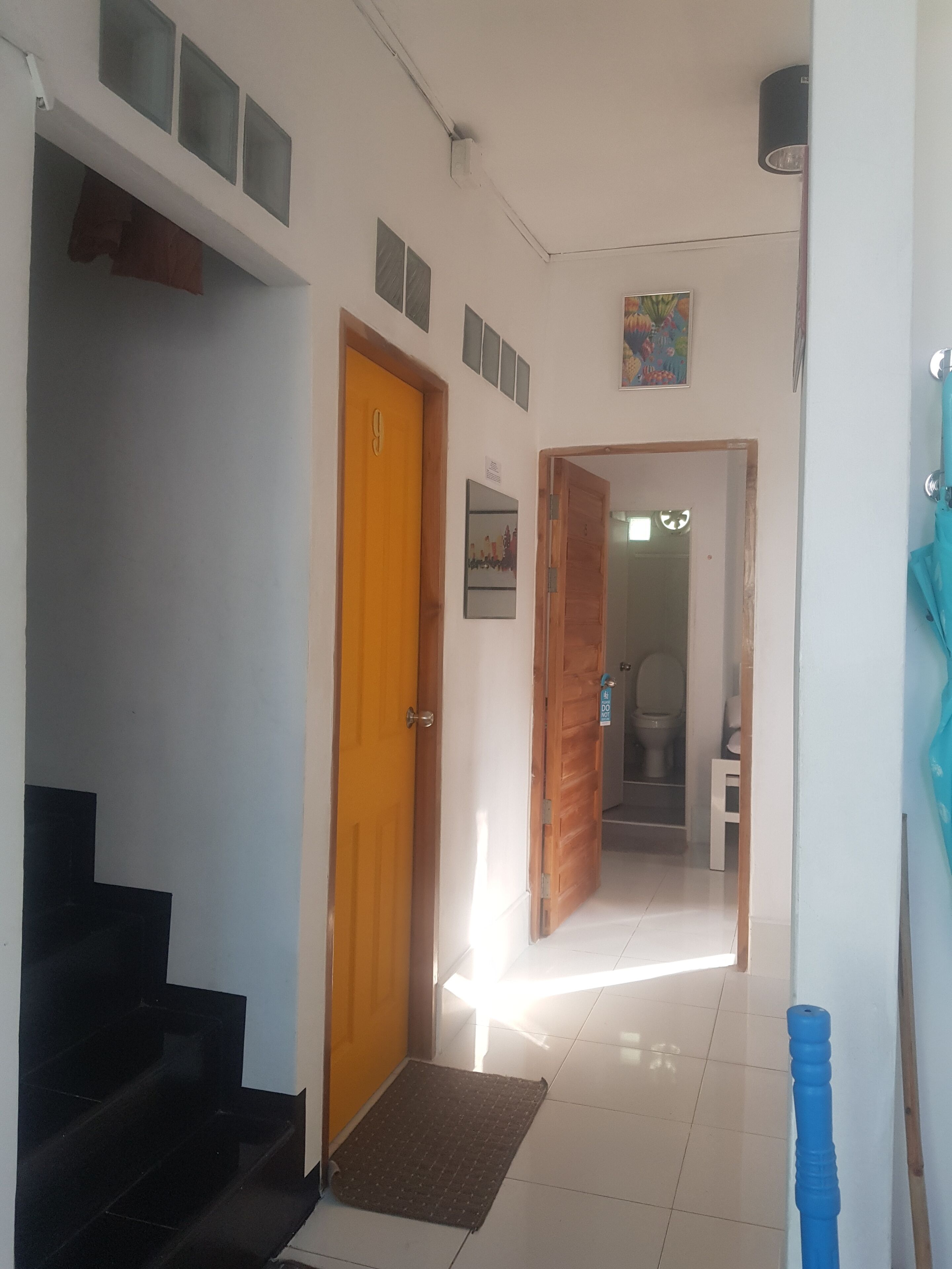 Un couloir avec une porte en bois, un escalier et une salle de bain visible à travers une porte ouverte.