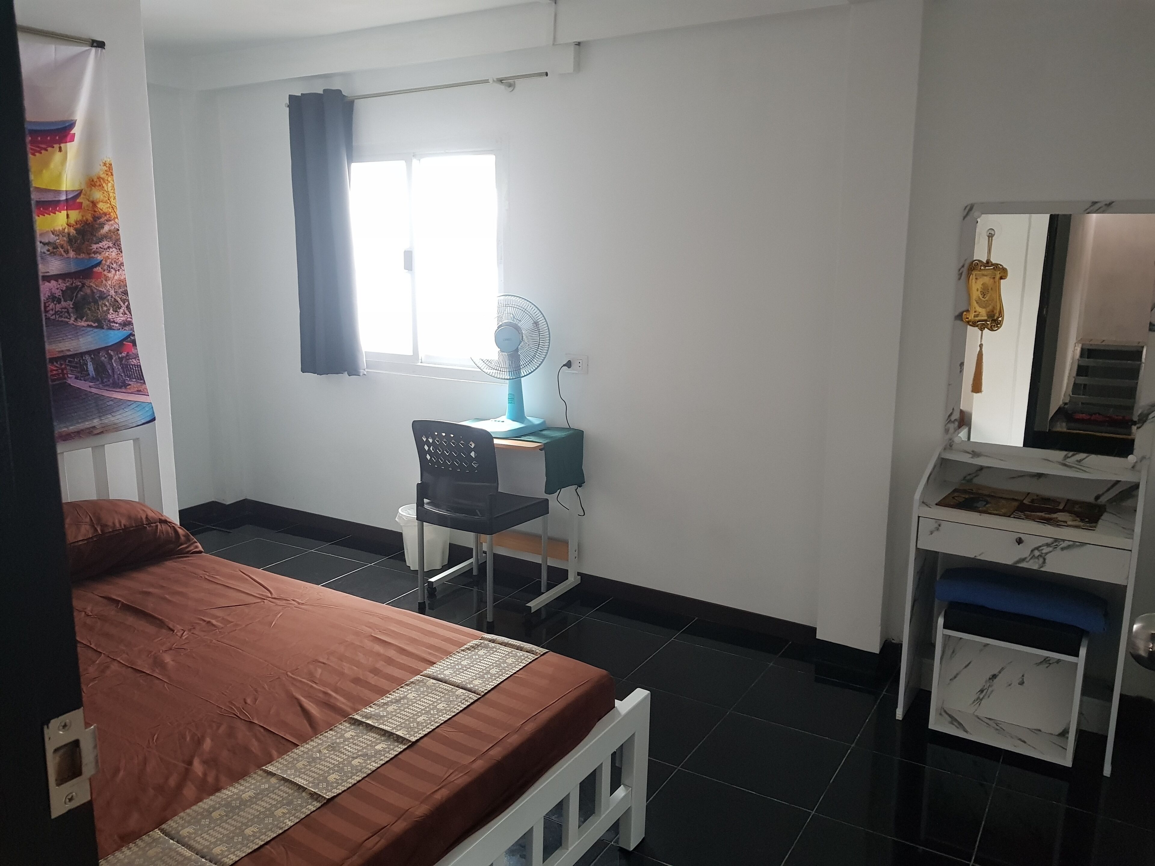 Quarto com cama, escrivaninha, cadeira, ventoinha e guarda-roupa.
