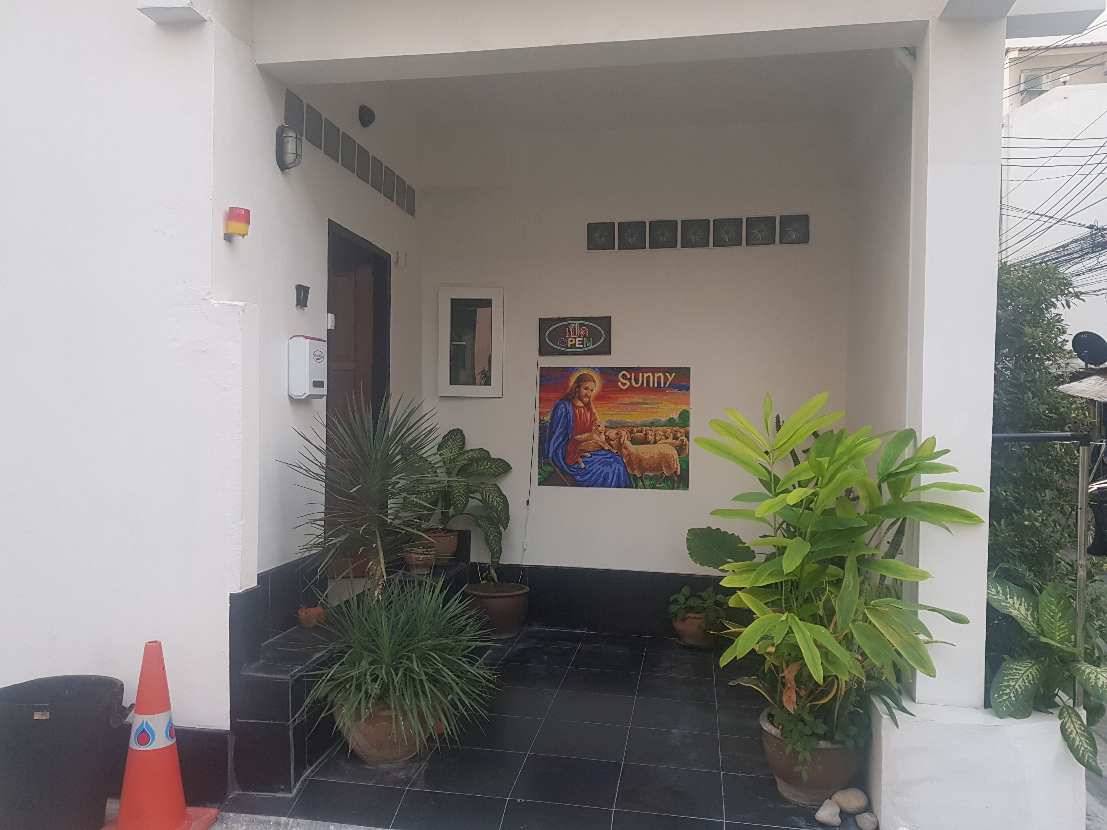 A clean, white exterior with a tiled entrance, potted plants, and a 'Sunny' poster.