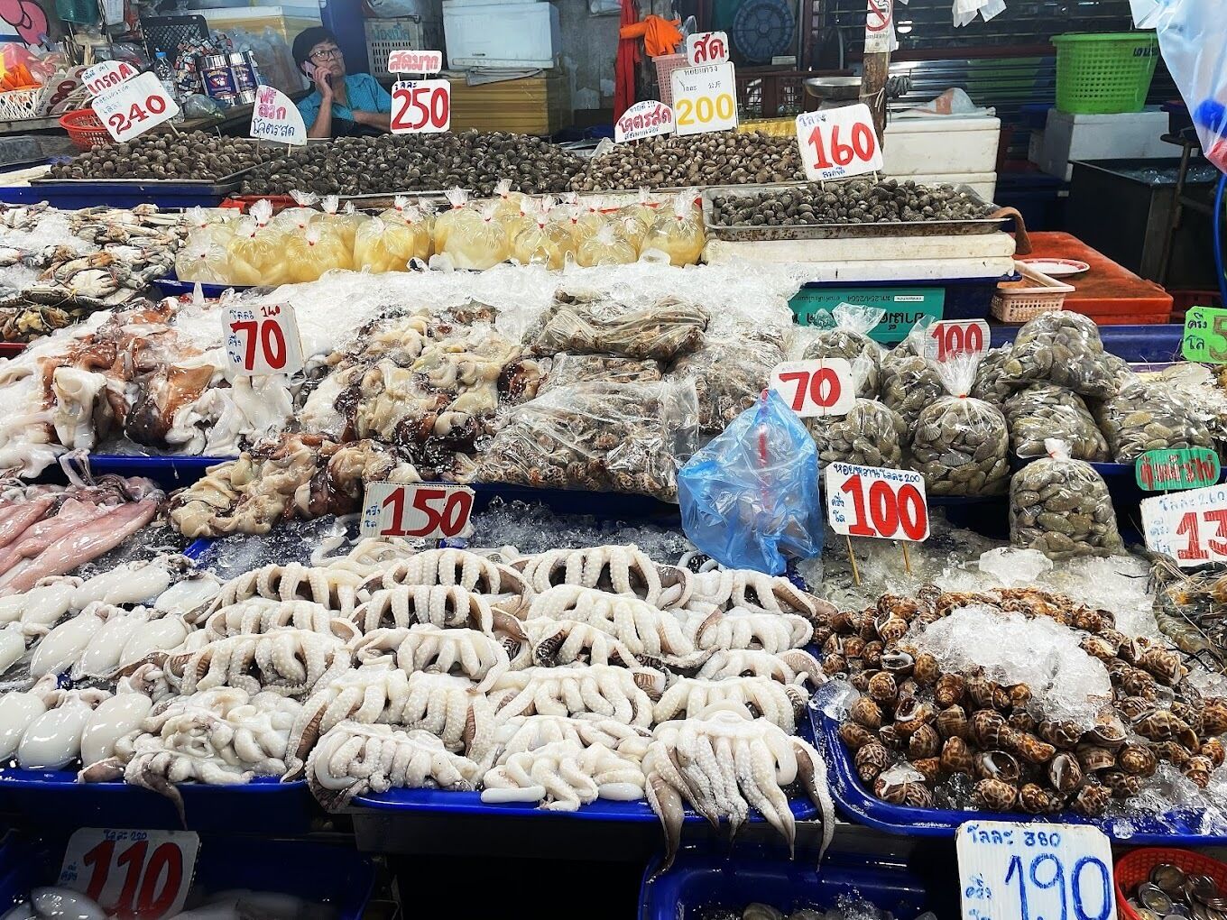 Un mercado de mariscos con diversos productos expuestos sobre hielo, como pulpo, almejas y otros mariscos, con etiquetas de precio visibles.