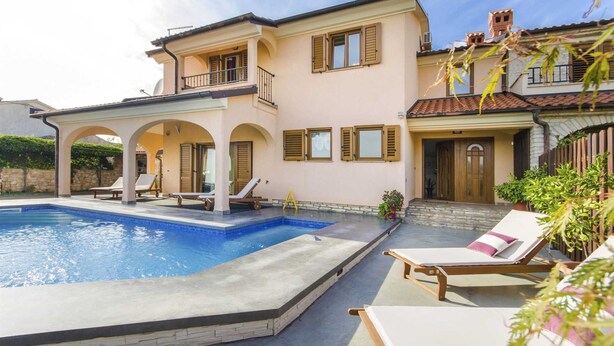 Une maison à deux étages avec une piscine, un espace salon extérieur et un mur en pierre.