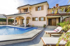 A two-story house with a swimming pool, outdoor seating, and a stone wall.