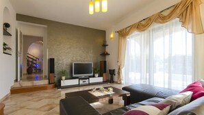 Un salon moderne avec un téléviseur à écran plat, un canapé, une table basse et une grande fenêtre avec des rideaux.