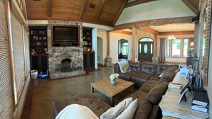 A spacious living room with a stone fireplace, leather sofa, and a television. - Family Home (Water Valley)