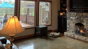 A spacious living room with a stone fireplace, large windows, and a high ceiling with exposed beams. - Family Home (Water Valley)