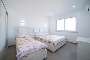 Two single beds with floral-patterned bedspreads, a white desk, and a large window.