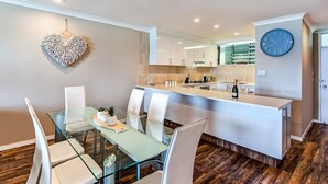 A modern kitchen with white cabinets, a central island, and a clock on the wall. - The Elite F208 by HamoRent on Hamilton Island (Hamilton Island)