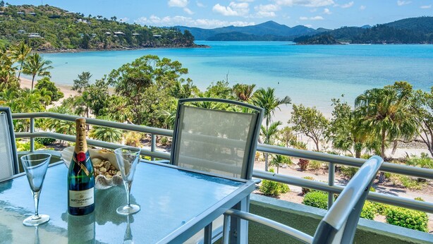 A table with a bottle of champagne, a glass, and nuts, overlooking a beach and turquoise waters. - The Elite F208 by HamoRent on Hamilton Island (Hamilton Island)