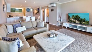 A modern living room with a sofa, coffee table, and TV. - The Elite F208 by HamoRent on Hamilton Island (Hamilton Island)