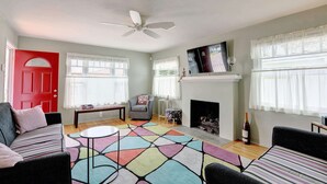 A living room with a red door, a fireplace, a ceiling fan, and a colorful rug.