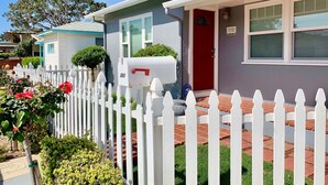 A row of single-story houses with white picket fences, a mailbox, and a red door.