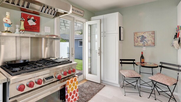 A modern kitchen with a stainless steel stove, a red and white sign, and two folding chairs.