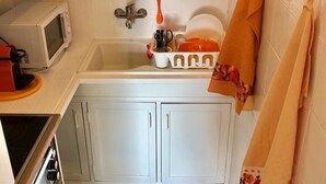 Una cocina con armarios blancos, microondas, pileta con escurreplatos y una toalla colgada en la pared.