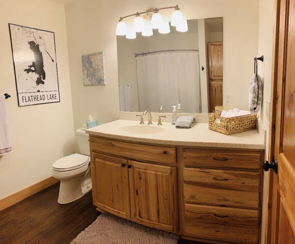 Une salle de bain avec un meuble-lavabo en bois, un évier, un miroir et des toilettes. Il y a une carte accroch ée au mur et un panier posé sur le meuble-lavabo.