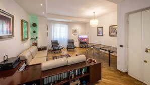 Uma sala de estar moderna com um sofá, duas poltronas, uma mesa de jantar com cadeiras, uma televisão e um lustre.