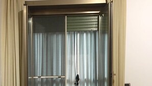 Quarto com porta de vidro deslizante para uma varanda, uma escrivaninha com computador e uma cama com colcha florida.