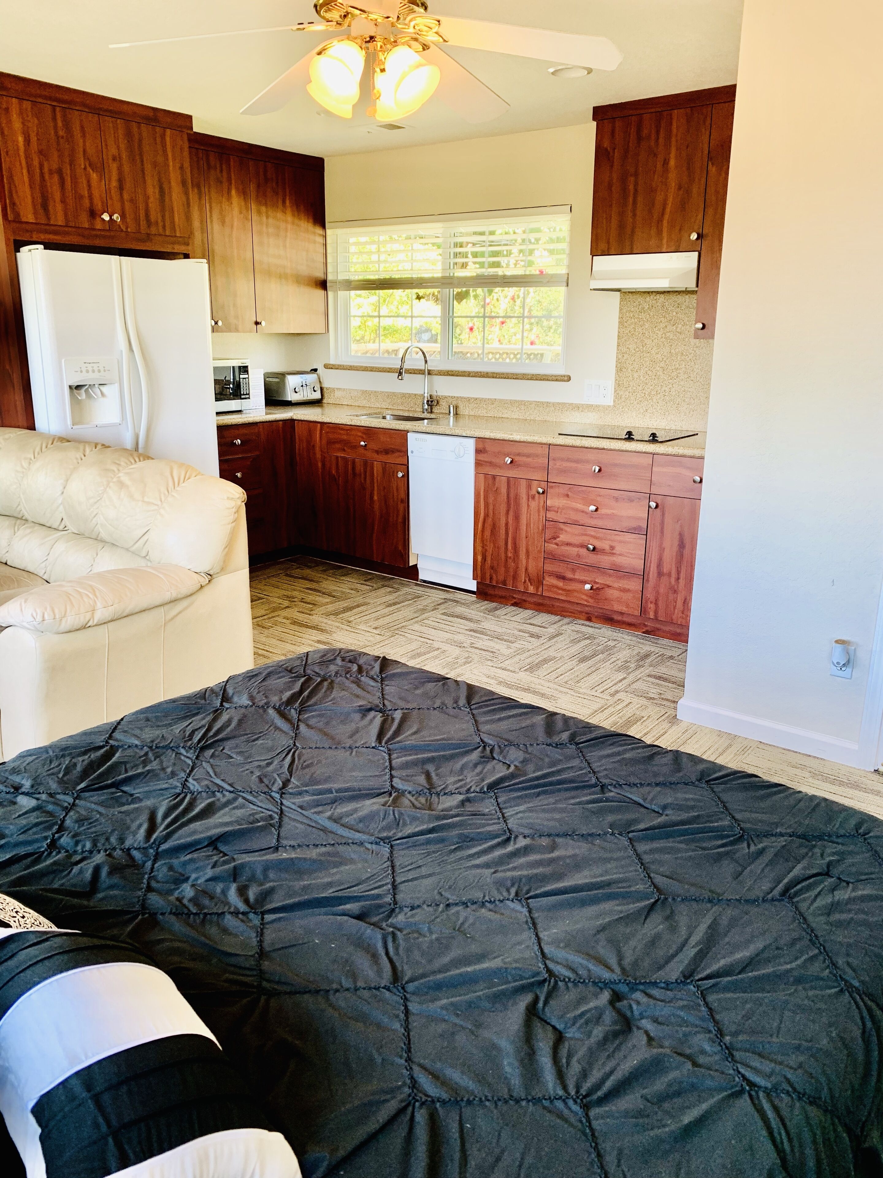 A compact bedroom with a bed, a kitchenette, and a ceiling fan.