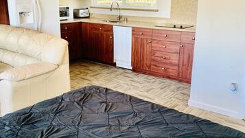 A compact bedroom with a bed, a kitchenette, and a ceiling fan.
