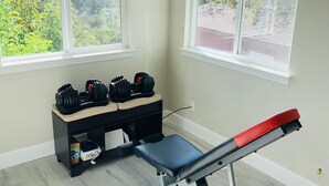 A room with a bench press, dumbbells, and a small table with boxes. - Views on a Hill..... (San Jose)