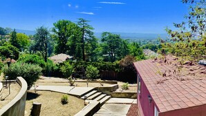 A residential property with a red-roofed building, a stone pathway, and a view of a green landscape with trees and distant hills. - Views on a Hill..... (San Jose)