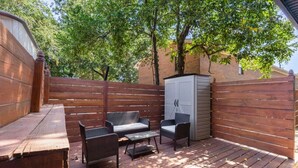 A wooden deck with a bench and two wicker chairs, a small table, and a shed.