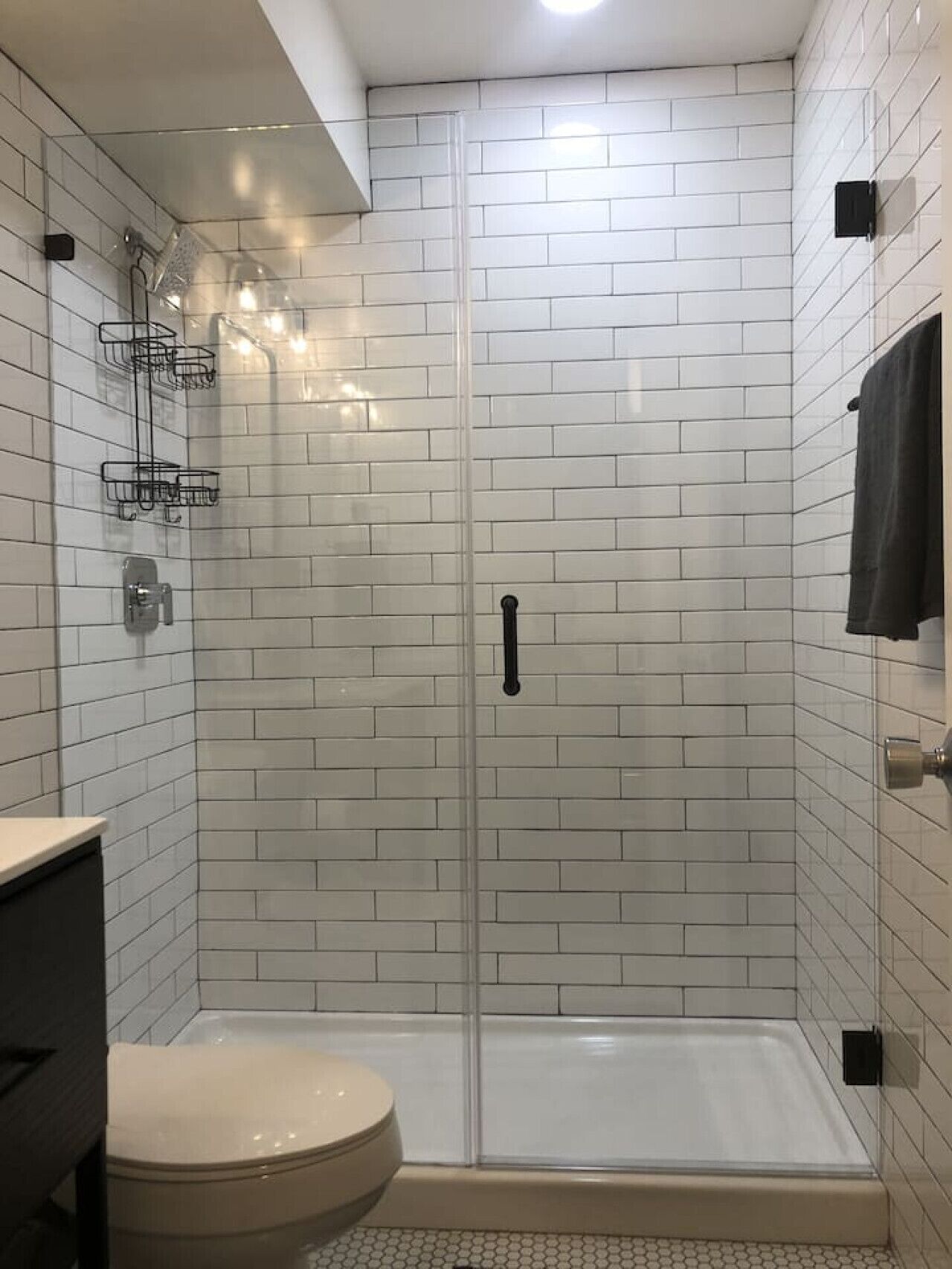 Een douche met glazen deur, witte betegelde wanden en een toilet links.