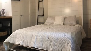 A bedroom with a bed, a TV mounted on the wall, and a ladder against the wall.