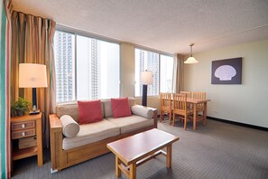 Une chambre d’hôtel avec un canapé, une table à manger et des chaises. Il y a deux lampes de chaque côté du canapé.